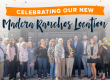 A large group of people stands smiling in front of a building under a banner that reads, Celebrating Our New Madera Ranchos Location. Confetti is falling in the background.
